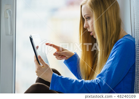 Young woman sitting at windowill using tablet 48240109
