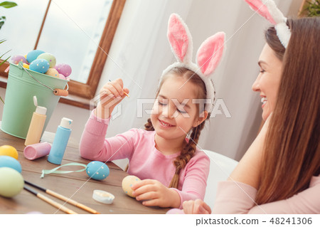 Mother and daughter together easter preparation at home sitting in bunny ears girl holding the brush Mother and daughter together easter preparation at home sitting in bunny ears girl holding the brush 48241306