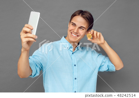 Freestyle. Teenager boy standing isolated on grey taking selfie on smartphone with cryptocurrency 48242514
