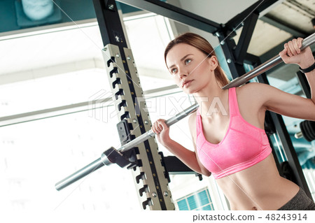 Young girl in gym healthy lifestyle standing with bar lifting weights concentrated close-up 48243914