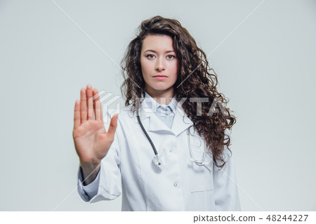 A young beautiful woman doctor gesturing stops. Probably a female doctor shows a gesture stop over a 48244227