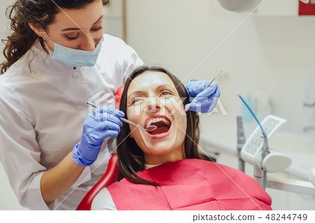 A young female doctor is dressed in a mask and medical gloves. During this, the patient receives a A young female doctor is dressed in a mask and medical gloves. During this, the patient receives a 48244749