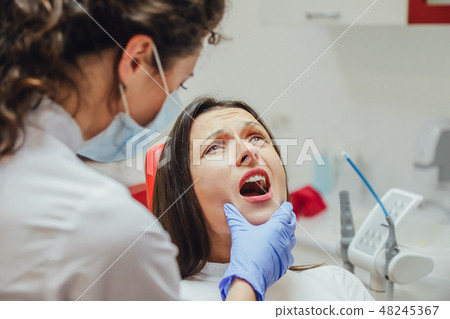 Young woman sitting in a dental chair for appointment of a doctor. During this time, she was very Young woman sitting in a dental chair for appointment of a doctor. During this time, she was very 48245367