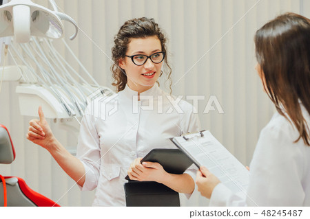 Portrait of a smiling dentist and assistant, looking at the clipboard in a modern dental clinic 48245487