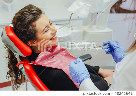 Woman at the reception of a dentist in a dental clinic. She sits in a red chair. Happy patient and Woman at the reception of a dentist in a dental clinic. She sits in a red chair. Happy patient and 48245641