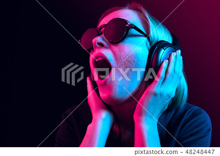 Fashion pretty woman with headphones listening to music over neon background Fashion pretty woman with headphones listening to music over neon background 48248447