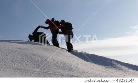 climbers hand in hand climb to top of a snowy mountain. the team of travelers in winter go to their 48251144