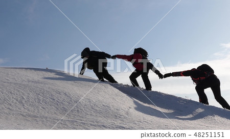 climbers hand in hand climb to top of a snowy mountain. the team of travelers in winter go to their climbers hand in hand climb to top of a snowy mountain. the team of travelers in winter go to their 48251151