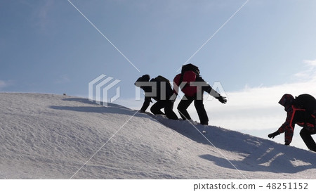 climbers hand in hand climb to top of a snowy mountain. the team of travelers in winter go to their 48251152