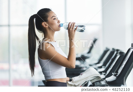 Woman drinking water after exercising on treadmill Woman drinking water after exercising on treadmill 48252110