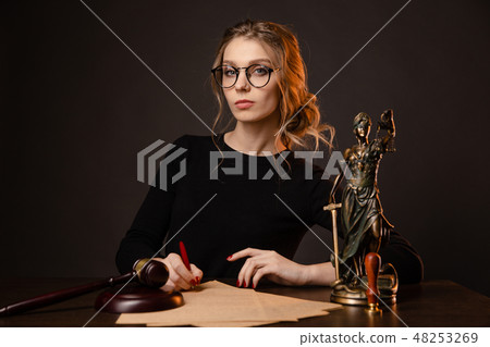 Young lawyer woman in a formal dress and spectacles sitting at table and writing something by pen 48253269