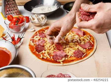 Man preparing pizza, decorating with salami and ham Man preparing pizza, decorating with salami and ham 48254221