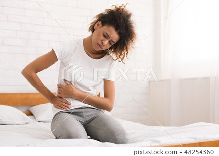 African-american girl suffering from abdominal pain on bed African-american girl suffering from abdominal pain on bed 48254360