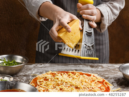 Woman sprinkling pizza with cheese, rubbing on grater 48255287