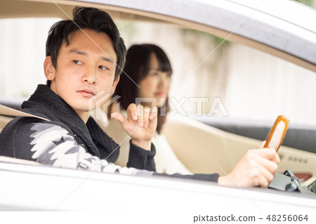 A male drabar who visually checks the car with the aria driving and judges the situation and a woman in the passenger seat that keeps calmness 48256064