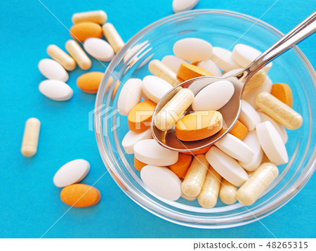 Pills in spoon and bowl on blue background Pills in spoon and bowl on blue background 48265315