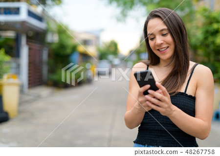 Young happy multi-ethnic woman using phone outdoors Young happy multi-ethnic woman using phone outdoors 48267758