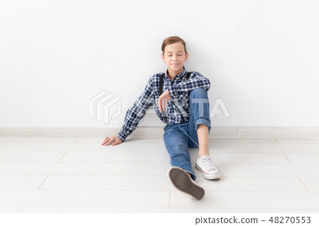 teenager, children and fashion concept - Fashionable boy sitting on floor over white background 48270553
