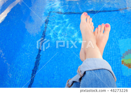 Crossed woman feet in blue jeans by swimming pool Crossed woman feet in blue jeans by swimming pool 48273226
