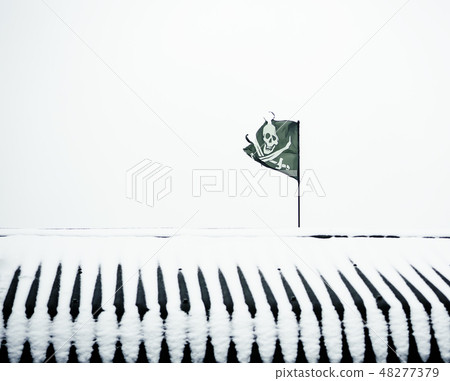 A ragged black pirate flag on a snow-covered roof. A ragged black pirate flag on a snow-covered roof. 48277379