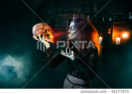 Scary witch holds human skull and reads the spell Scary witch holds human skull and reads the spell 48277974