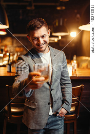Smiling man stretches out glass of alcohol in bar 48278012