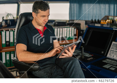 chief officer on navigation bridge watching digital tablet. chief officer on navigation bridge watching digital tablet. 48279726
