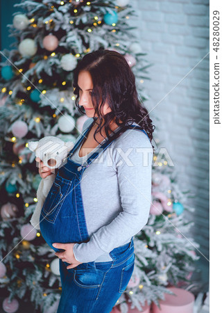 A beautiful pregnant young girl in a blue denim overalls holds a bear in her hands and looks at him A beautiful pregnant young girl in a blue denim overalls holds a bear in her hands and looks at him 48280029