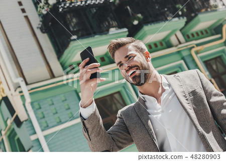 I'm only in the mood for good news today. Smiling brown-haired man standing outdoors and using his 48280903