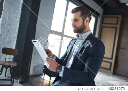 Working hard Confident and young businessman in stylish suit is using his tablet for work 48281073