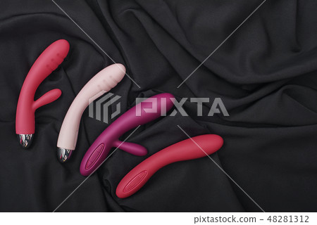 Discover a sexier you. Collection of colorful G-spot vibrators arranged on a black silk fabric. 48281312