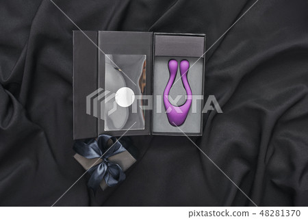 Unique design. Close up of purple sex toy for her and black gift box on a black silk fabric Unique design. Close up of purple sex toy for her and black gift box on a black silk fabric 48281370