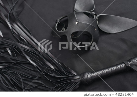 Impress him. Top view of bdsm leather kit (black whip and mask) against of a black silk. Impress him. Top view of bdsm leather kit (black whip and mask) against of a black silk. 48281404