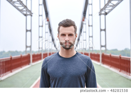 Serious about sport. Handsome young man in sports clothing looking at camera while standing on the Serious about sport. Handsome young man in sports clothing looking at camera while standing on the 48281538