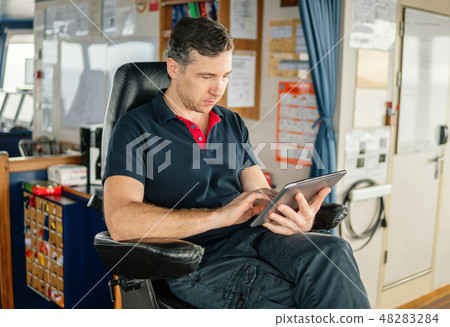 chief officer on navigation bridge watching digital tablet. chief officer on navigation bridge watching digital tablet. 48283284