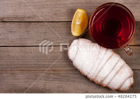 Cup of tea with croissant sprinkled with powdered sugar on old wooden background with copy space for Cup of tea with croissant sprinkled with powdered sugar on old wooden background with copy space for 48284275