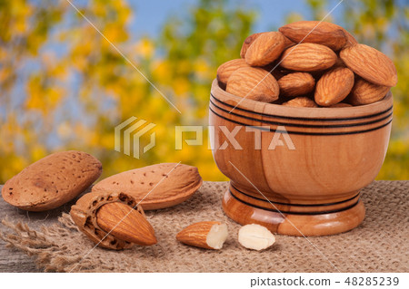 almonds in a bowl on the old wooden board with sackcloth and blurred garden background 48285239