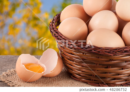 eggs in a wicker basket on a wooden board with blurred garden background 48286732