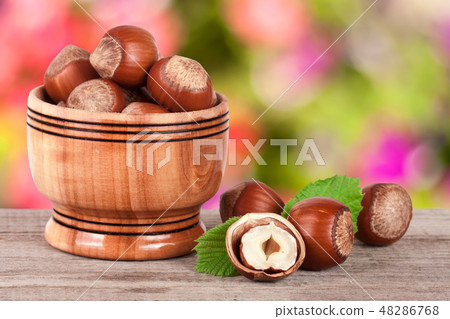 Hazelnuts with leaves in a wooden bowl on a wooden table with blurred garden background Hazelnuts with leaves in a wooden bowl on a wooden table with blurred garden background 48286768