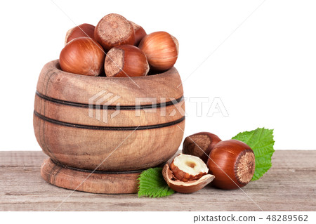 Hazelnuts with leaves in a wooden bowl on a wooden table with a white background Hazelnuts with leaves in a wooden bowl on a wooden table with a white background 48289562