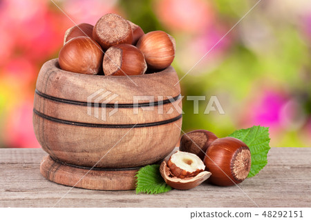 Hazelnuts with leaves in a wooden bowl on a wooden table with blurred garden background Hazelnuts with leaves in a wooden bowl on a wooden table with blurred garden background 48292151