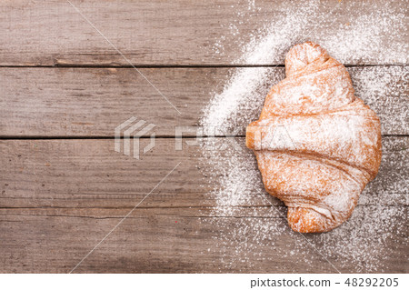 one croissant sprinkled with powdered sugar on old wooden background with copy space for your text one croissant sprinkled with powdered sugar on old wooden background with copy space for your text 48292205