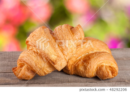 two croissant on a wooden board with a blurry garden background 48292206