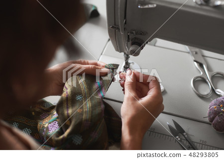 Seamstress working on modern electrical sewing machine making exclusive garments in fashion studio. Seamstress working on modern electrical sewing machine making exclusive garments in fashion studio. 48293805