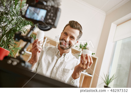 Online shopping. Cheerful young male blogger recording new video blog episode about new cosmetic Online shopping. Cheerful young male blogger recording new video blog episode about new cosmetic 48297332