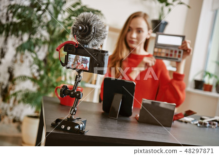 Beauty tips. Young attractive woman showing a makeup palette on camera while recording video review Beauty tips. Young attractive woman showing a makeup palette on camera while recording video review 48297871