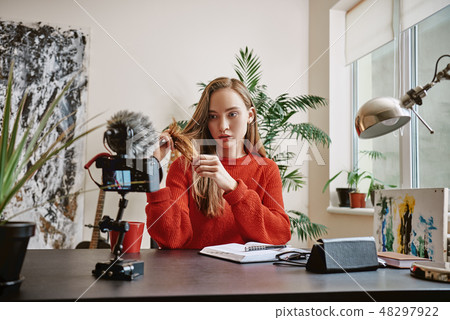 Beauty expert. Attractive young blogger talking about daily hair care with tripod mounted digital Beauty expert. Attractive young blogger talking about daily hair care with tripod mounted digital 48297922