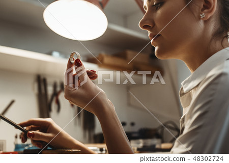 Perfection. Close up of young female jeweler looking and inspecting a ring. 48302724
