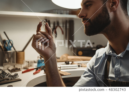 My precious. Close up of young male jeweler looking and inspecting a ring. My precious. Close up of young male jeweler looking and inspecting a ring. 48302743