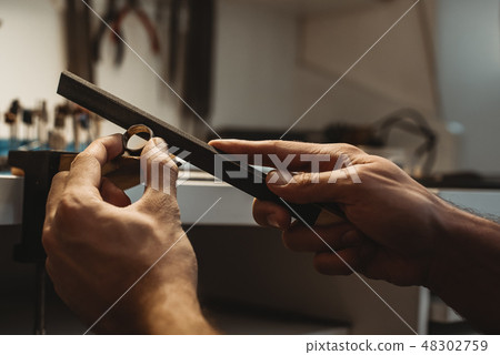 Creating a masterpiece. Close up of a male jeweler's hands working and shaping an unfinished ring Creating a masterpiece. Close up of a male jeweler's hands working and shaping an unfinished ring 48302759